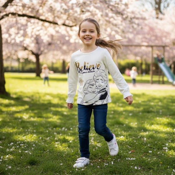 Niña sonriendo en parque con ropa de La Giralda y cerezos en flor.