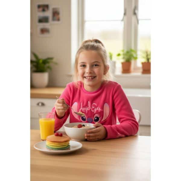 Niña sonriendo desayunando cereales y fruta en cocina luminosa.